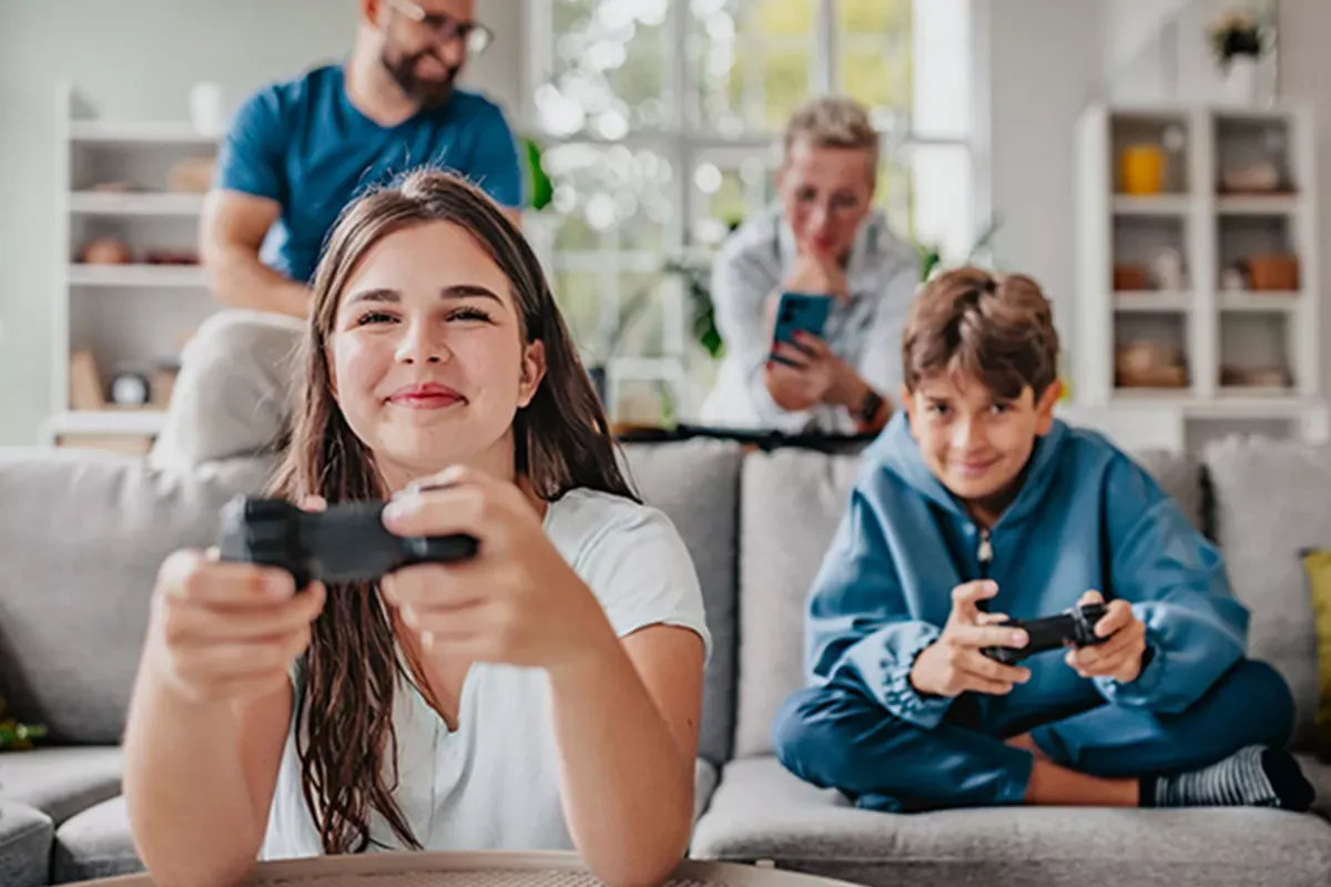 Siblings gaming while parents use phones in the background